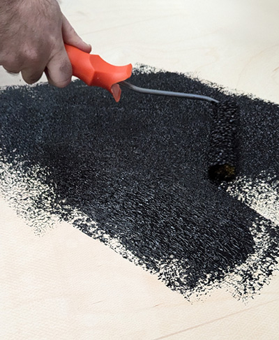 action shot of black Armacab speaker paint being rolled onto wooden panel