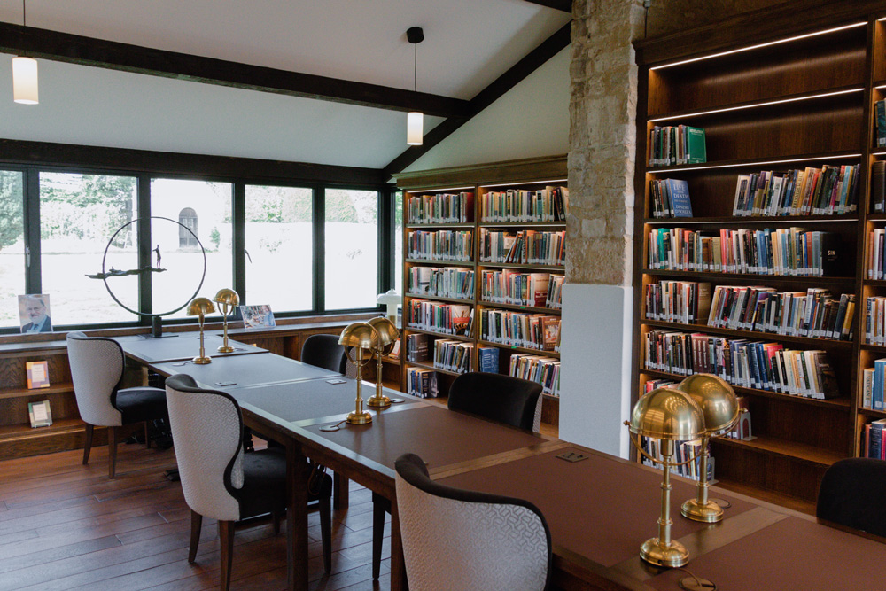Desks and chairs with large window and gold desk lamps infront of wooden shelving unit with books